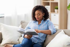 Woman sitting on a sofa and reading a book before she leaves a review