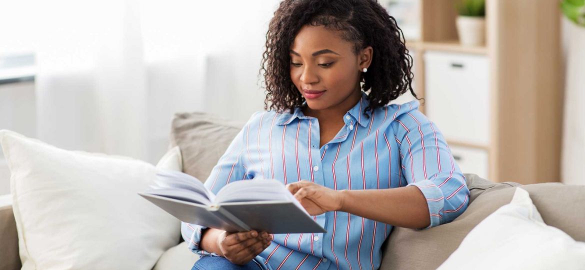 Woman sitting on a sofa and reading a book before she leaves a review